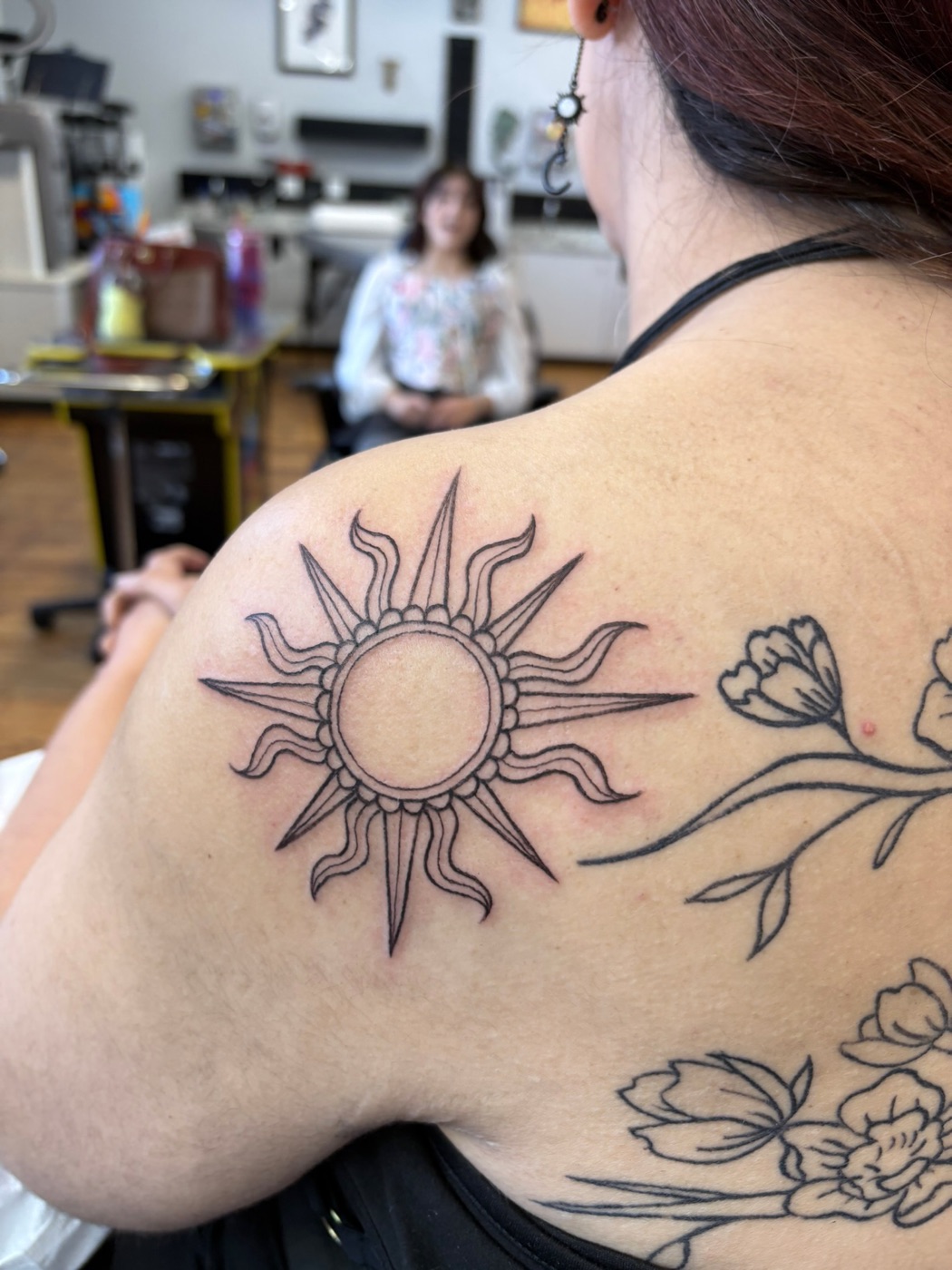 Ornate sun with wildflowers fine line tattoo by Caitlyn Barbosa